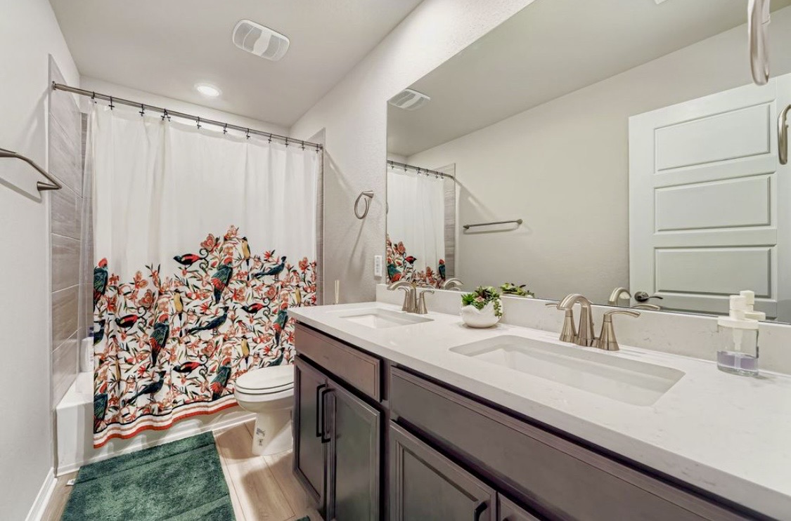 A second bathroom at HIS House with a double vanity and floral shower curtain